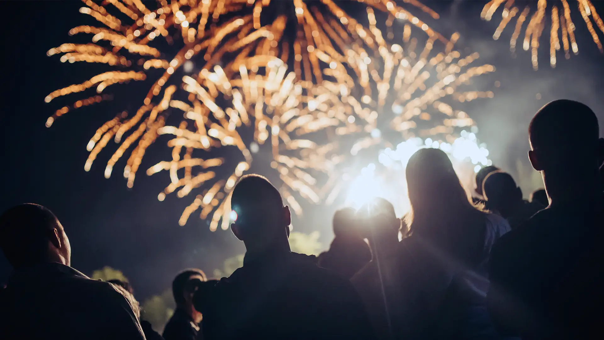 Fyrverkerier lyser upp natthimlen över ett bostadsområde, sett från säkert avstånd utanför hyreshusen